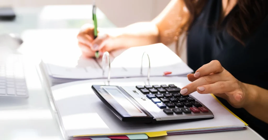 Close-up of a woman using a calculator and taking notes on financial documents, illustrating accounting or financial planning.