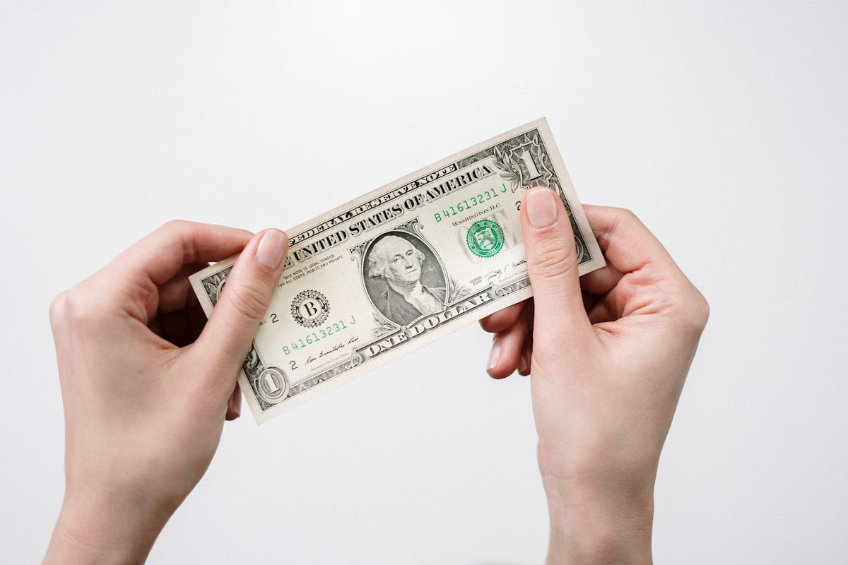 Hands holding a single US dollar bill, symbolizing the debate around income tax and the question: Is Trump getting rid of income tax.