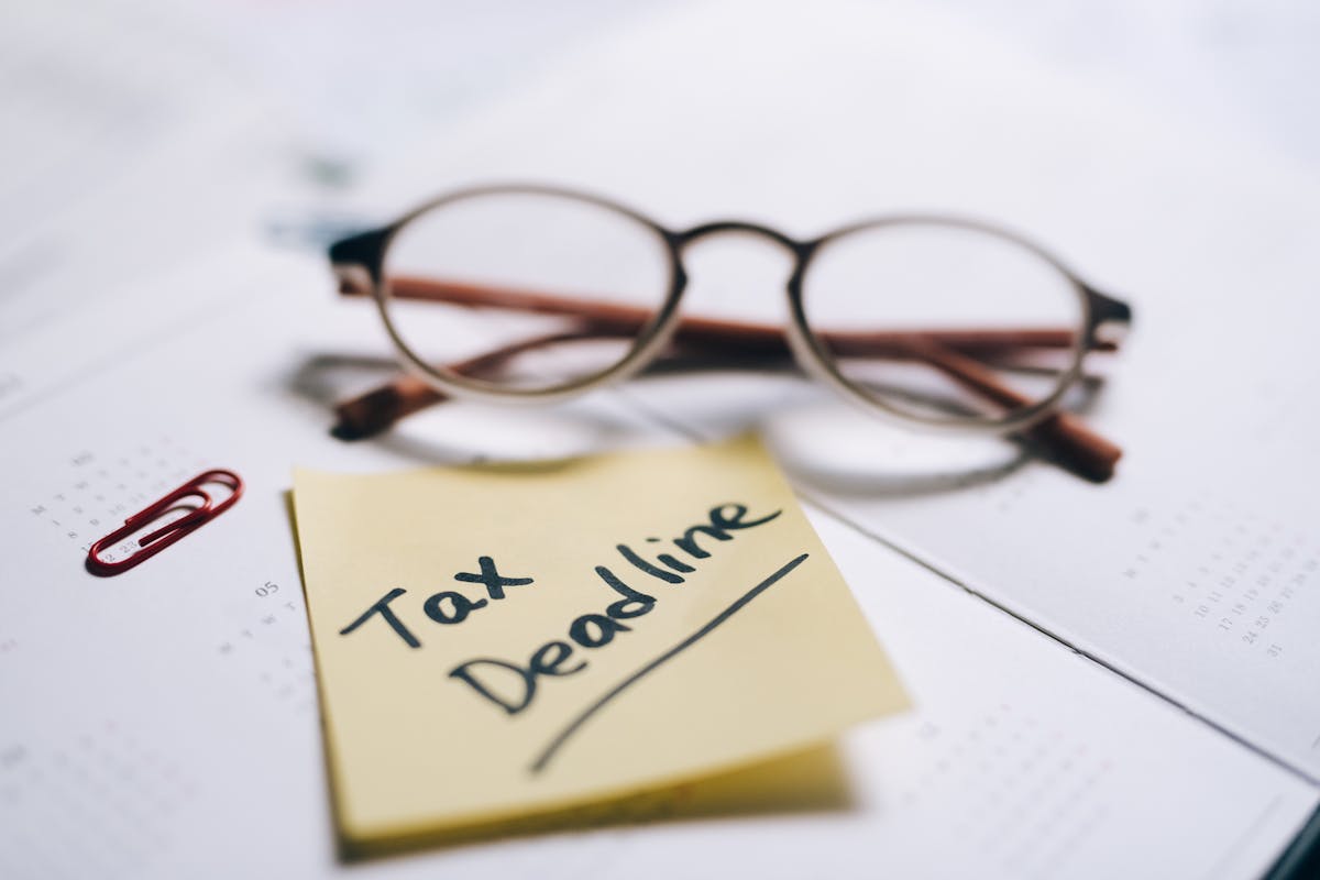 Sticky note labeled 'Tax Deadline' on a calendar next to glasses, reminding about the tax extension deadline 2025.