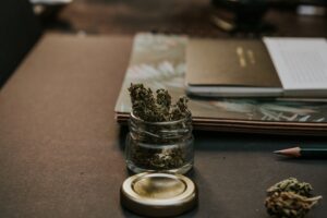Florida cannabis excise tax is represented by a small glass jar filled with cannabis buds on a desk with notebooks and a pencil nearby.