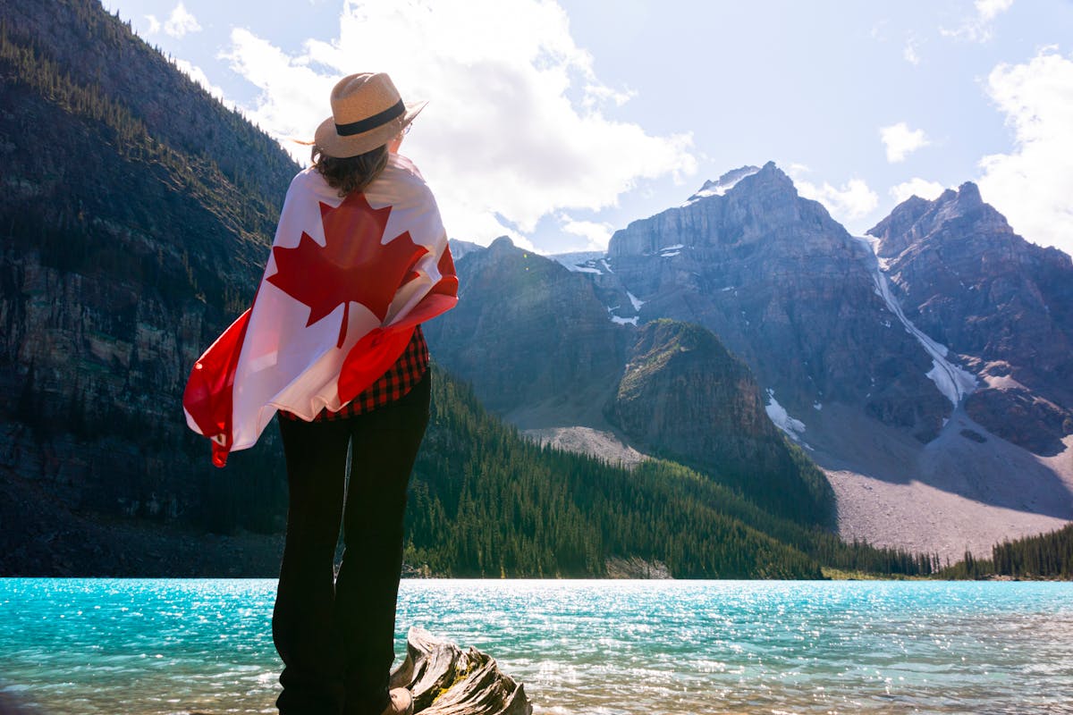 How to immigrate to Canada, shown by a scenic lakeside vista with a person wearing the Canadian flag.
