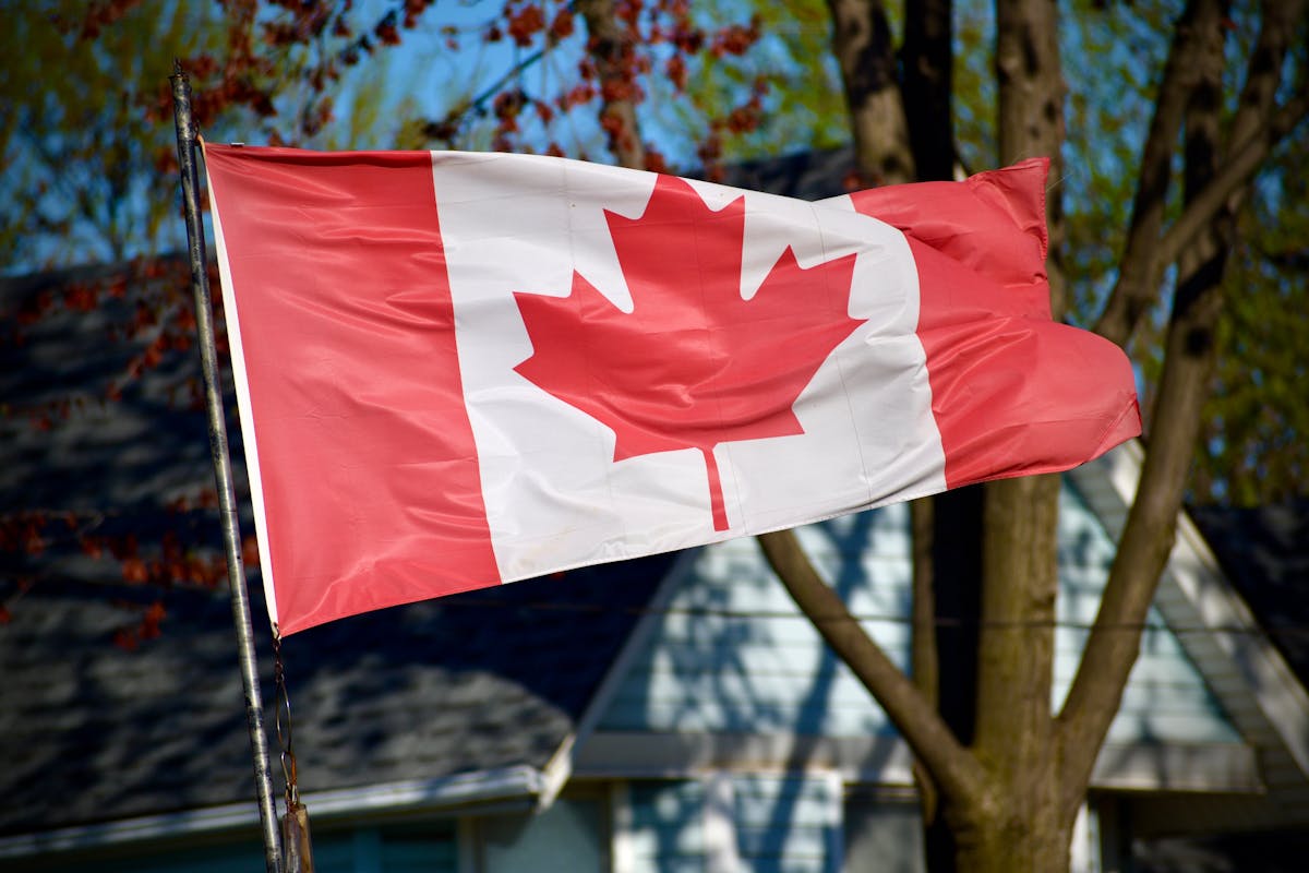 Moving to Canada from the US shown by Canada’s national flag against trees and houses.